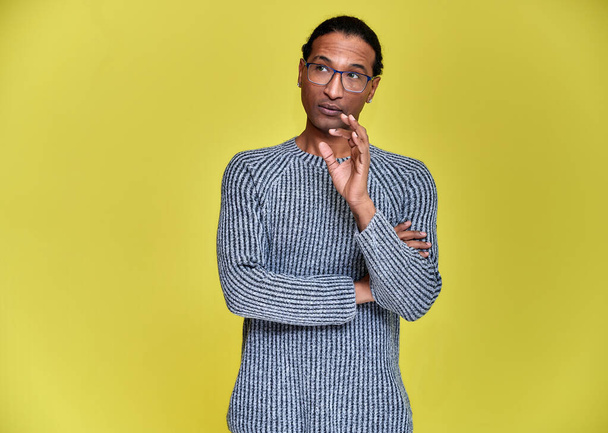 Portrait of a young African American man in glasses with a short haircut and with a white-toothed smile in a gray sweater on a yellow background. Standing and talking right in front of the camera. - Photo, image