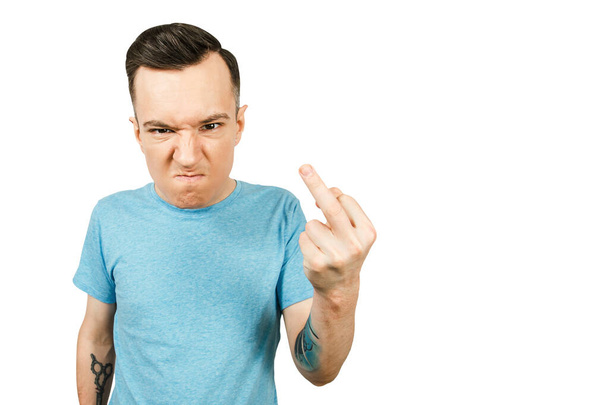 Молодой мрачный парень показывает средний палец знак трахаться, одетый в синюю футболку на изолированном белом фоне
. - Фото, изображение