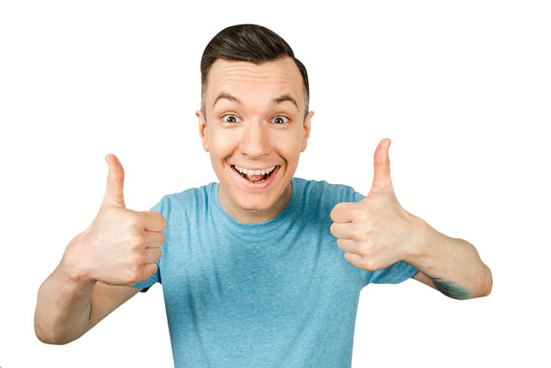 Young smiling guy, dressed in a blue t-shirt, show thumbs up on a isolated white background. - Photo, Image