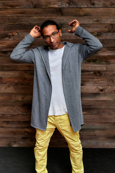 Vertical Portrait Young man with short-haired African-American glasses in ordinary clothes on a vintage wooden background in a home interior in a loft style. Standing right in front of the camera - Foto, Bild