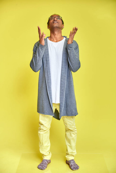 Vertical portrait of a cheerful young man wearing glasses African-American with a short haircut in ordinary clothes on a yellow background in full length. Standing right in front of the camera - Фото, изображение