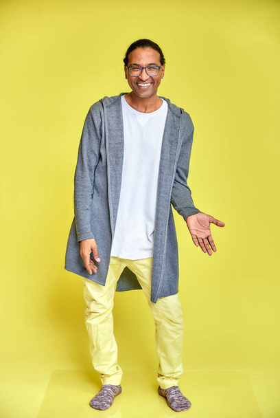Vertical portrait of a cheerful young man wearing glasses African-American with a short haircut in ordinary clothes on a yellow background in full length. Standing right in front of the camera - Foto, afbeelding