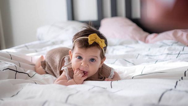 Little infant baby girl portrait lying on bed with yelow bow on head - Fotografie, Obrázek