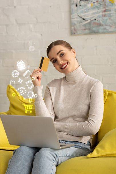 Smiling girl with credit card and laptop looking at camera near illustration - Foto, afbeelding