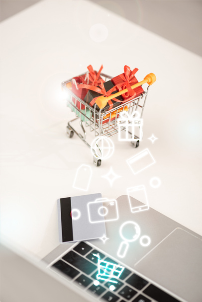 Selective focus of toy gifts in cart beside laptop and credit card and illustration - Foto, Imagem