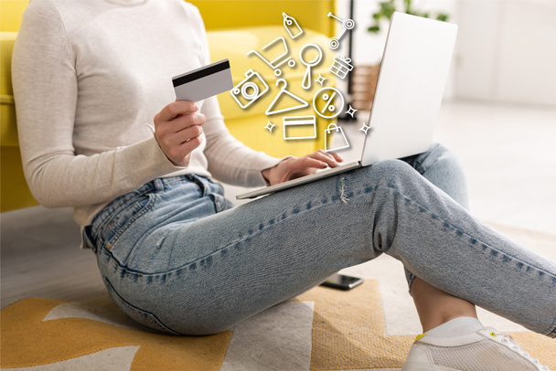 Cropped view of young woman holding credit card and using laptop near illustration - Photo, Image