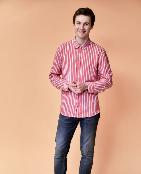 vertical portrait of a young Caucasian man with short hair and a white-toothed smile in a pink shirt on a pink background. Standing and talking right in front of the camera showing hands. - Valokuva, kuva
