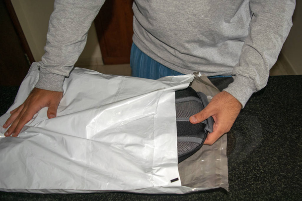 Человек, открывающий доставку пластиковой посылки с новым рюкзаком. Онлайн доставка пластиковой упаковки. Почтовая служба
  - Фото, изображение
