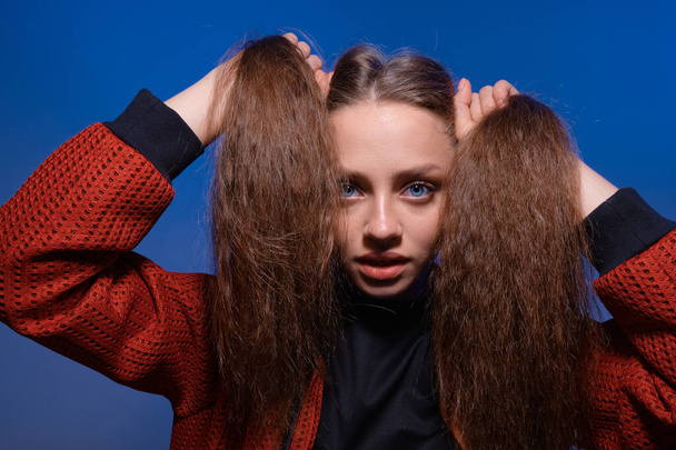 Cute teenager girl making ponytails holding hair with hands, posing in studio with blue background. - Foto, Imagem