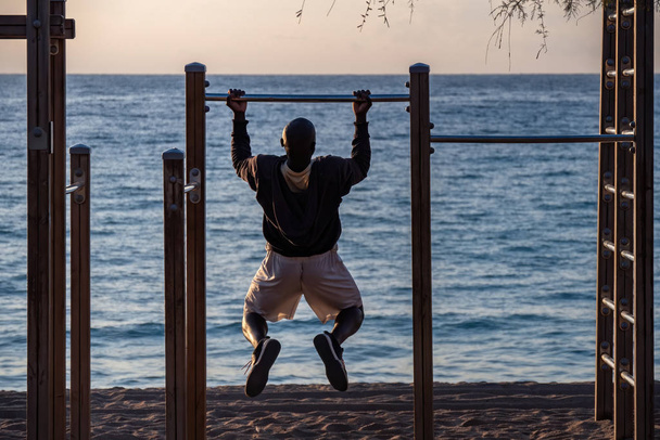 Afro man doet pull-ups op horizontale bar op het strand. Sport en Lifestyle. - Foto, afbeelding