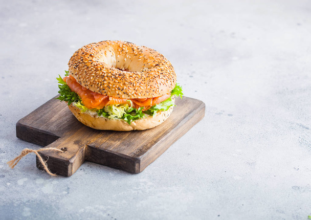 Fresh healthy bagel sandwich with salmon, ricotta and lettuce on vintage chopping board on stone kitchen table background. Healthy diet food. Space for text - Foto, immagini