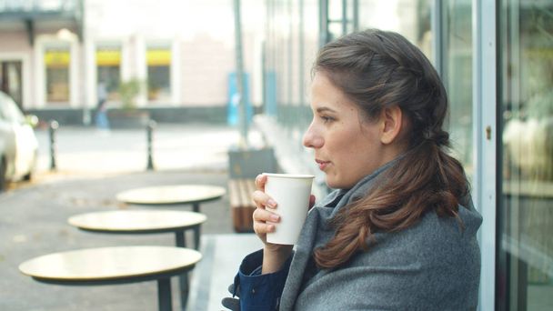Oldalnézet, fiatal nő becsomagolja magát egy szürke takaróba és kávét iszik. - Fotó, kép