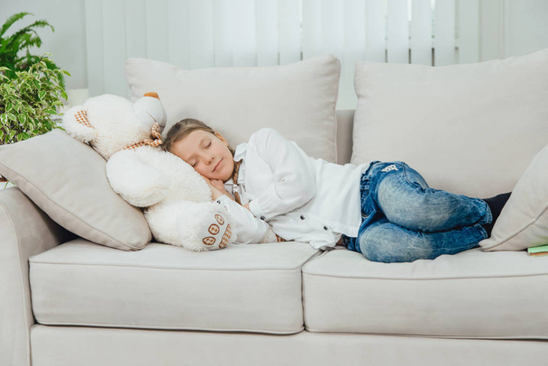 Sweet charming kid is lovely sleeping on her big white teddy-bear. Full-length. - Фото, зображення