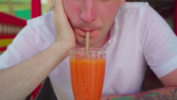 Cocktail de hombre bebiendo en la cafetería. Cama adulta bebiendo fruta fresca a través de paja mientras se sienta a la mesa en el restaurante de la calle el día soleado. - Metraje, vídeo