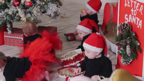Little babies sitting on the carpet and playing with christmas gifts - a boy crying - Materiał filmowy, wideo
