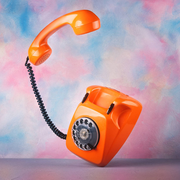 Vintage orange telephone on a bright colorful background - Фото, изображение