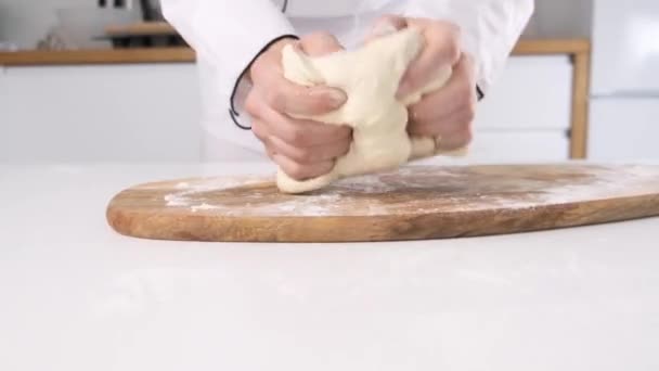 Mains masculines pétrissant la pâte dans la farine sur une table et une planche en bois. Gros plan
. - Séquence, vidéo