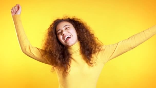 Young cute girl smiling and dancing on yellow studio background. Woman in colorful bright wear. Positive mood. Slow motion. - Кадри, відео