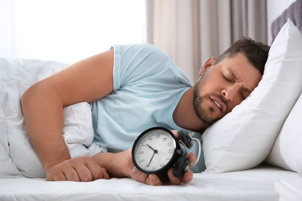 Sleepy man with alarm clock at home in morning - Foto, Imagen