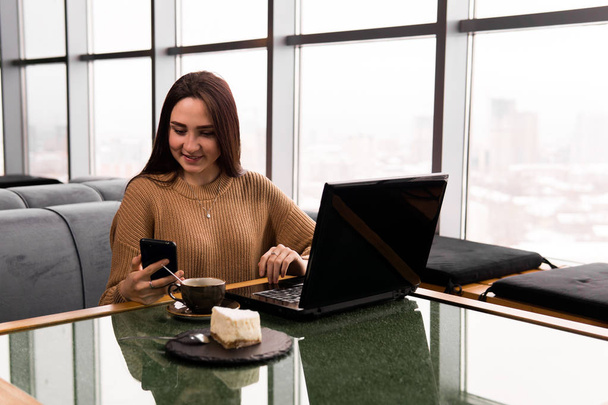 mujer joven trabaja con el ordenador portátil y smartphone en una cafetería
 - Foto, Imagen