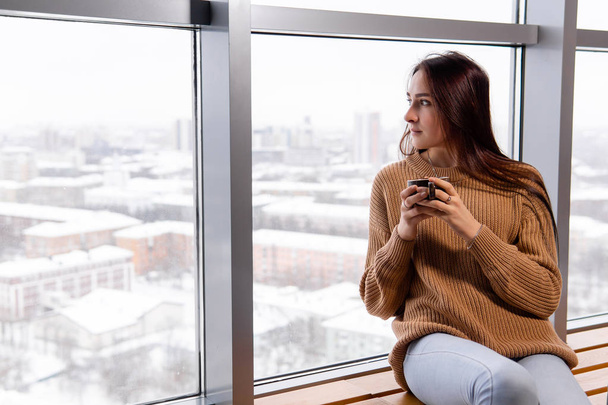 jonge vrouw met een kopje koffie zit bij het raam op de top f - Foto, afbeelding