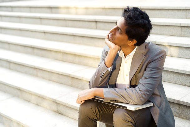 Young handsome Indian man in an office suit and white shirt sitting on the steps - Foto, imagen