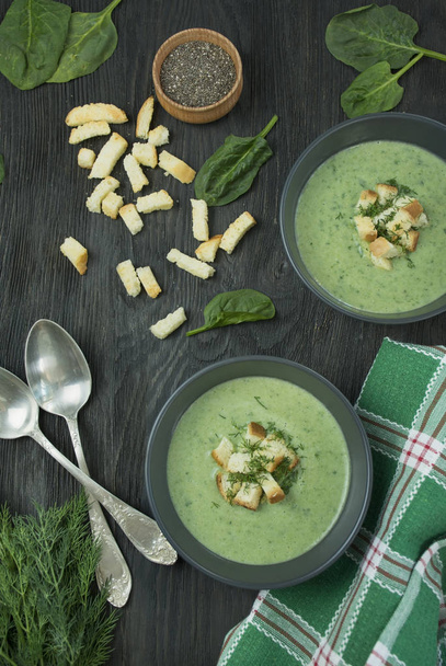 Creamy spinach soup with crackers, herbs and chia seeds. Green soup served in a bowl on a wooden table. Flat lay. - Photo, Image