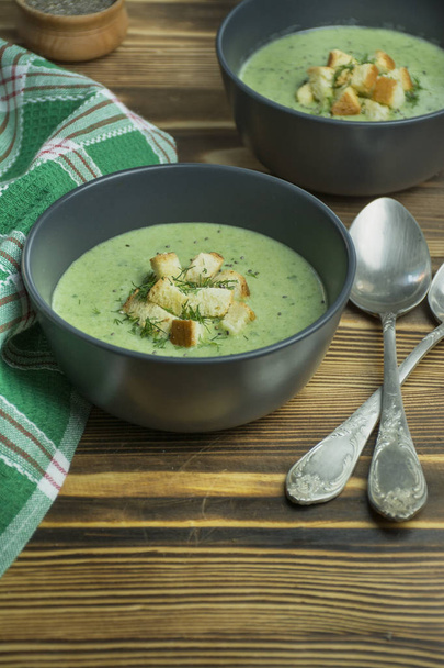 Сливочный шпинатный суп с крекерами, травами и семенами чиа. Зеленый суп подается в миске на деревянном столе
. - Фото, изображение