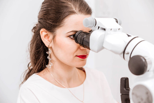 attraktive junge Zahnärztin im weißen Anzug benutzt bei der Arbeit ein Mikroskop - Foto, Bild