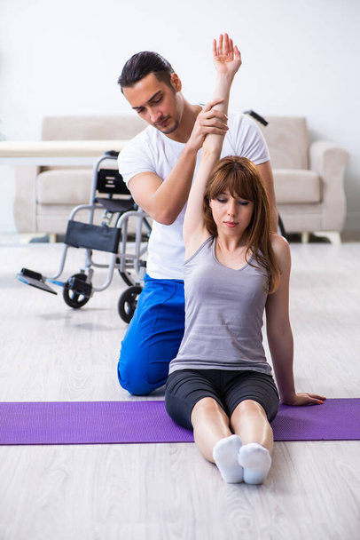 Male physiotherapist doing exercises with injured woman on floor - 写真・画像