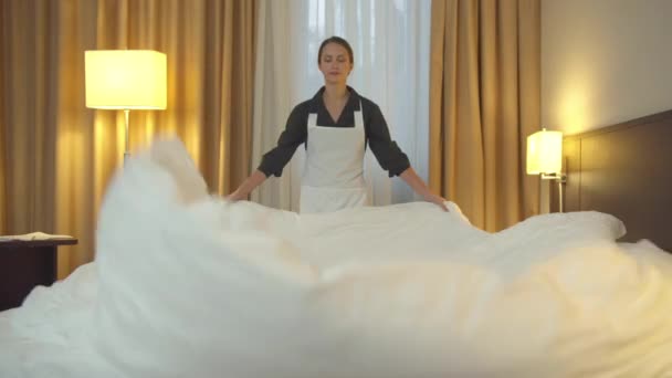 Pokojówka w mundurze pościeli łóżko i rozłożyli koc w pokoju hotelowym  - Materiał filmowy, wideo