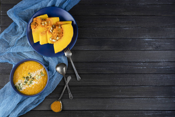 pumpkin cream soup in a ceramic bowl on a dark wooden background using blue textile, slices of pumpkin. flat lay. copy space. - Foto, Imagen