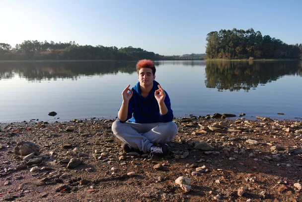 Jovem fazendo ioga e meditando perto de uma margem do lago
 - Foto, Imagem