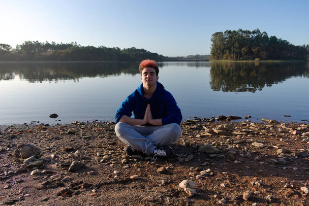 Młody człowiek uprawia jogę i medytuje nad brzegiem jeziora - Zdjęcie, obraz