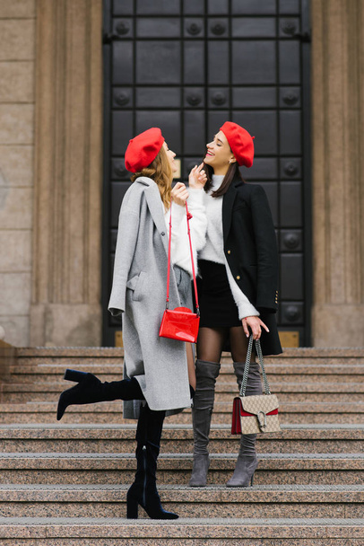 meninas brilhantes elegantes namoradas em boinas vermelhas e casacos de outono caminhar pela cidade e rir
 - Foto, Imagem