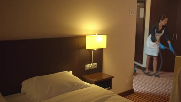 Pokojówka w mundurze odkurzanie podłogi w pokoju hotelowym - Materiał filmowy, wideo