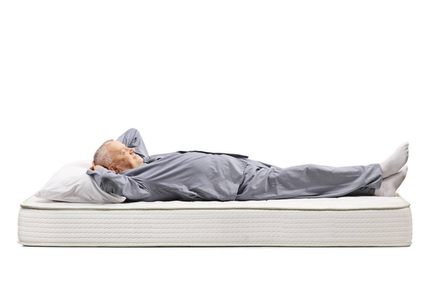 Mature man in pyjamas lying on a mattress - Fotoğraf, Görsel