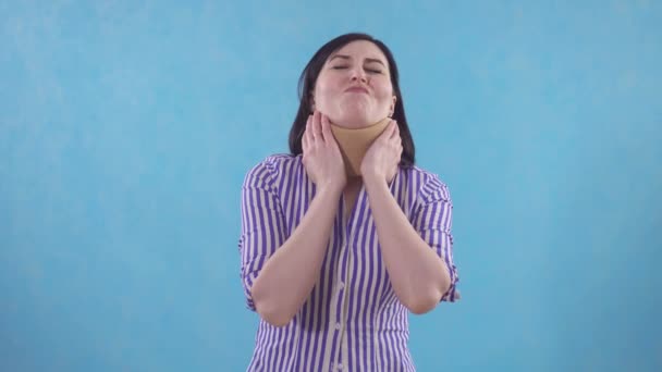 Young woman in protective collar against neck pain standing on blue background - Felvétel, videó