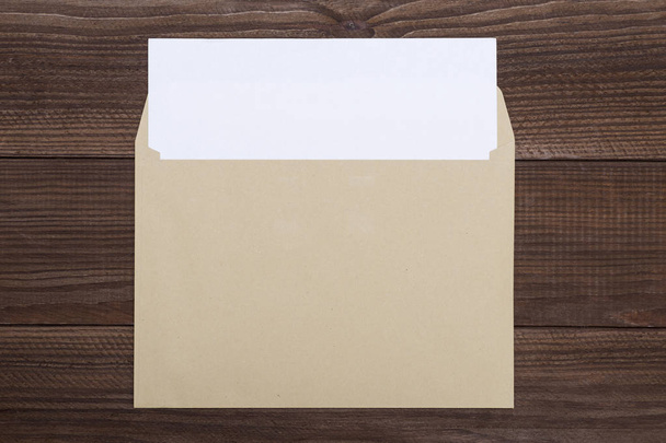 Tahta masada boş beyaz kart ve zarf. Ahşap zemin üzerinde beyaz kağıt olan açık, parlak, sarı bir zarf. - Fotoğraf, Görsel