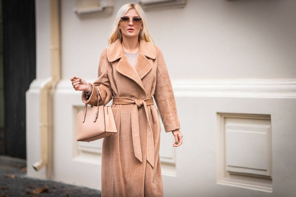 Young beautiful blond woman in an autumn coat stands on a city street. Soft focus. Fashionable concept. - Foto, imagen