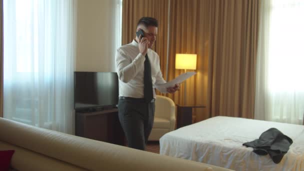 Muž v košili a kravatě vejít do pokoje v hotelu, mluvit po telefonu a podívat se na dokumenty - Záběry, video