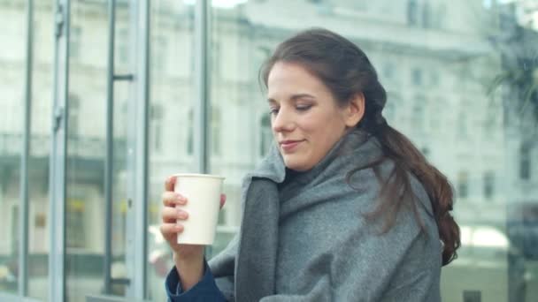 Girl wraps herself in a grey blanket and drinks coffee in a cafe  - Materiał filmowy, wideo