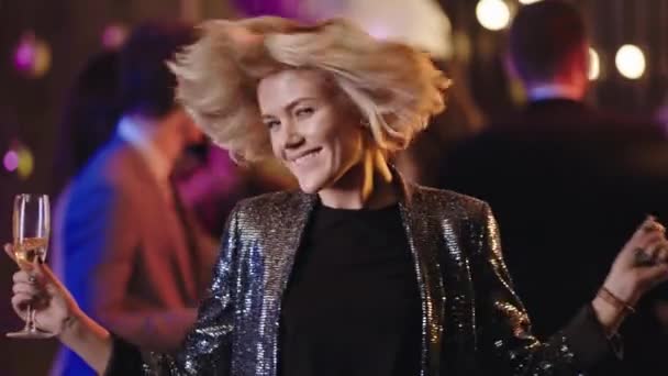 Šťastná a vzrušená blondýnka drží sklenici šampaňského a tančí vzrušeně před kamerou na velké párty, potřásá hlavou a vychutnává si okamžik - Záběry, video