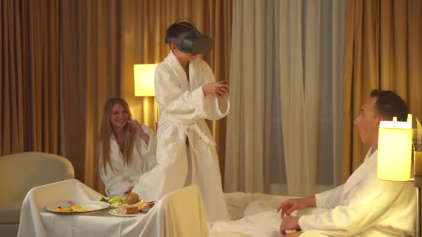 Οικογένεια στο δωμάτιο του ξενοδοχείου, ο μικρός γιος παίζει με γυαλιά εικονικής πραγματικότητας - Πλάνα, βίντεο
