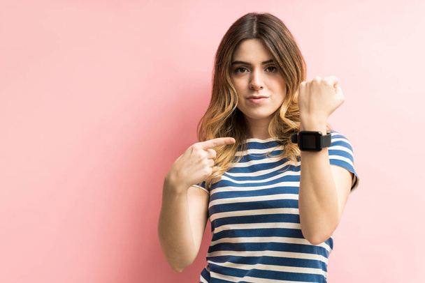 Mujer joven confiada mostrando su reloj inteligente mientras está de pie sobre el fondo de color
 - Foto, Imagen