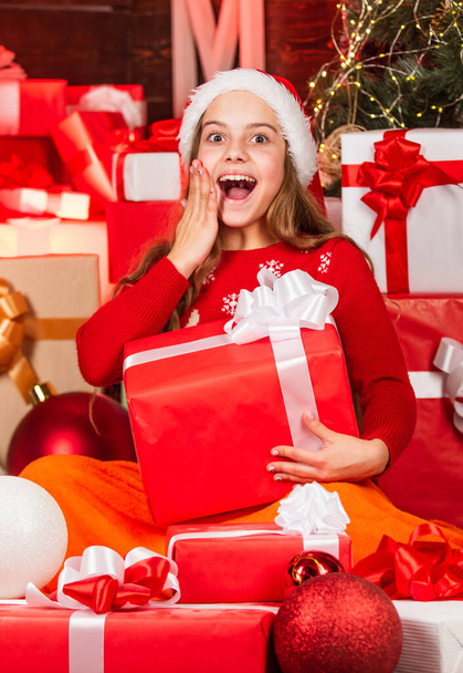 kid in santa hat with many gift boxes. successful shopping on xmas market. decorated with gifts. shopping packages christmas sale. cheerful santa helper sort presents. smiling shop assistant - Fotó, kép