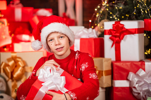 Kíváncsivá tett cuki Mikulás. A kis boldog fiú ajándékokat talál a karácsonyfa közelében. Ajándékbolt. Gyerek Mikulás kalap karácsonyi ajándékdobozok. Boldog karácsonyt! A tél szépsége. Szabadidő és aktivitás. Boksz nap - Fotó, kép