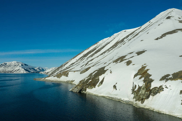 The mountainous sea coast covered with snow in a sunny weather. - Foto, afbeelding