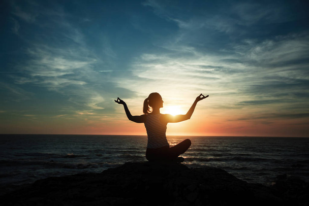 Силует жінки-йоги, що медитує на океанському пляжі під час чудового заходу сонця
. - Фото, зображення