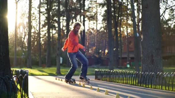 A sports bearded guy on rollers makes various turns between training cones, accidentally overturning one of them. Professional training of a man in slow motion on roller skates in the autumn. - Footage, Video